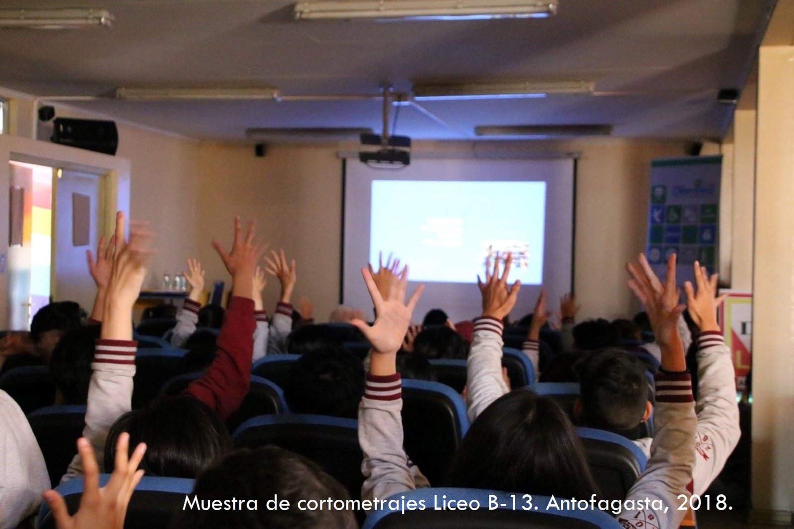 Estudiantes escolares levantando sus manos viendo muestra de cortometrajes en liceo